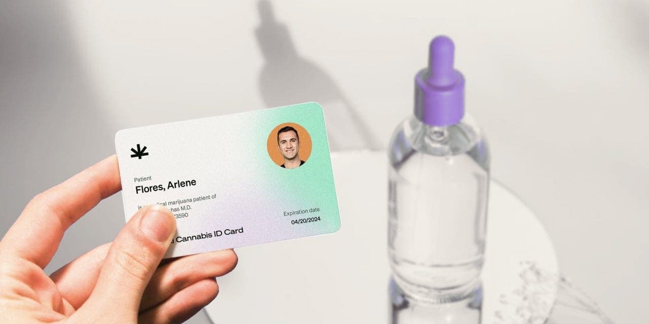 closeup of hand holding a medical marijuana card and a CBD oil on the background